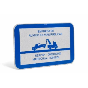Placa reflectante homologada V-24 para grúas de auxilio en vías públicas, con borde azul, pictograma de remolque y espacio para el número REAV y matrícula.