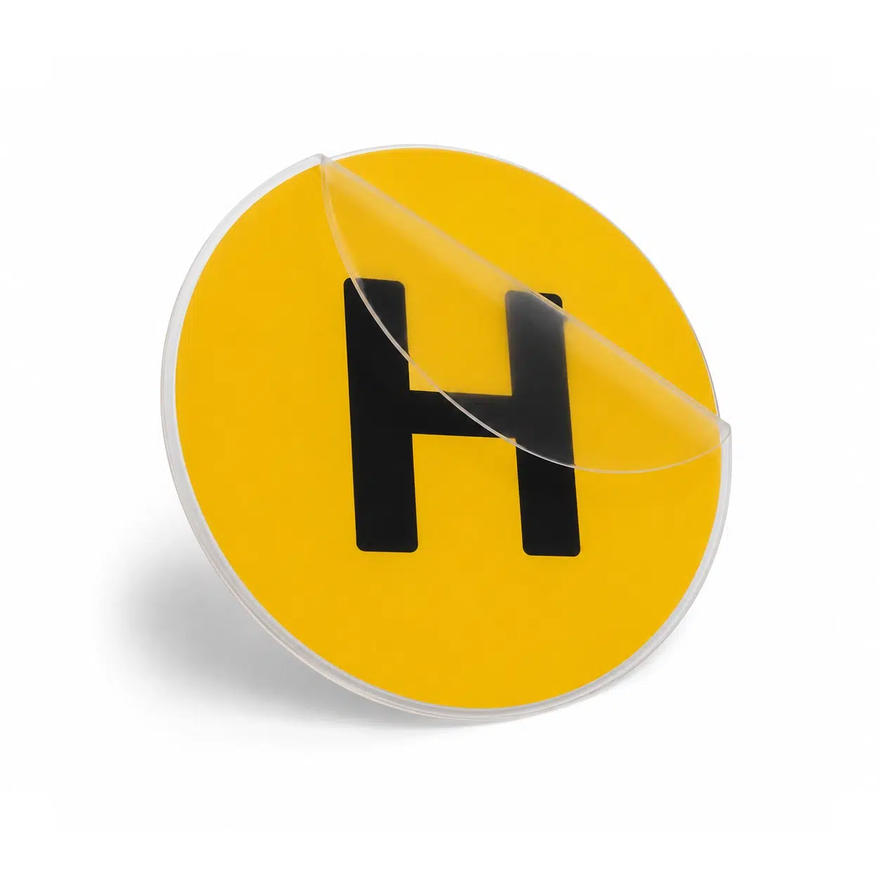 Distintivo 'H' Vehículo Histórico - Adhesivo 60mm Pegatina circular amarilla con la letra H mayúscula en negro para vehículos históricos, mostrando el plástico transparente transportador medio despegado.