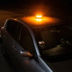 Baliza V16 conectada Metalight emitiendo una potente luz ámbar intermitente sobre el techo de un coche aparcado en la carretera de noche.