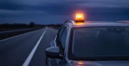 baliza v16 geolocalizada encendida en el techo de un coche gris oscuro detenido en el arcén al anochecer