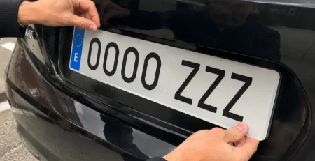 Mecánico instalando una nueva placa de matrícula acrílica en un coche para sustituir la antigua y superar la ITV.